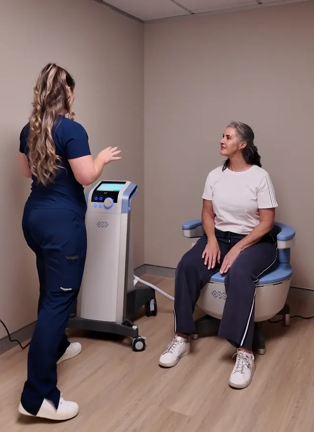 Our nurse talking with a woman seated fully clothed on the Emsella chair