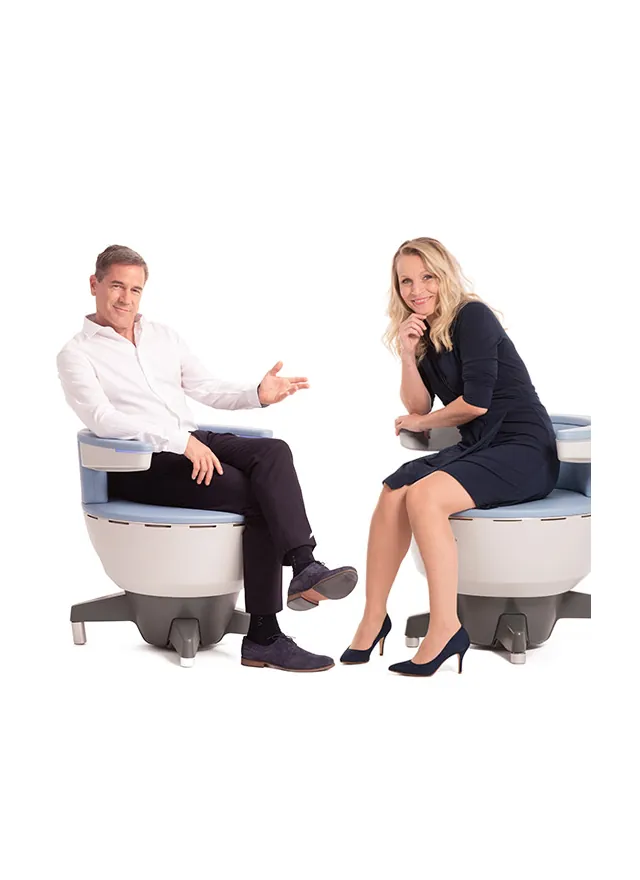 A man and a woman seated fully clothed on Emsella chairs